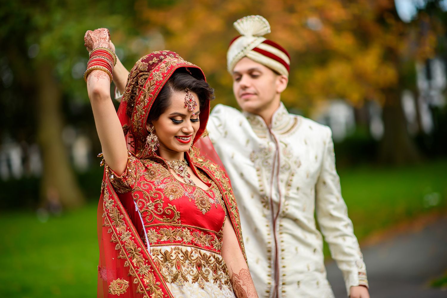 Couple in traditional Indian wedding attire posing in an autumn park setting.