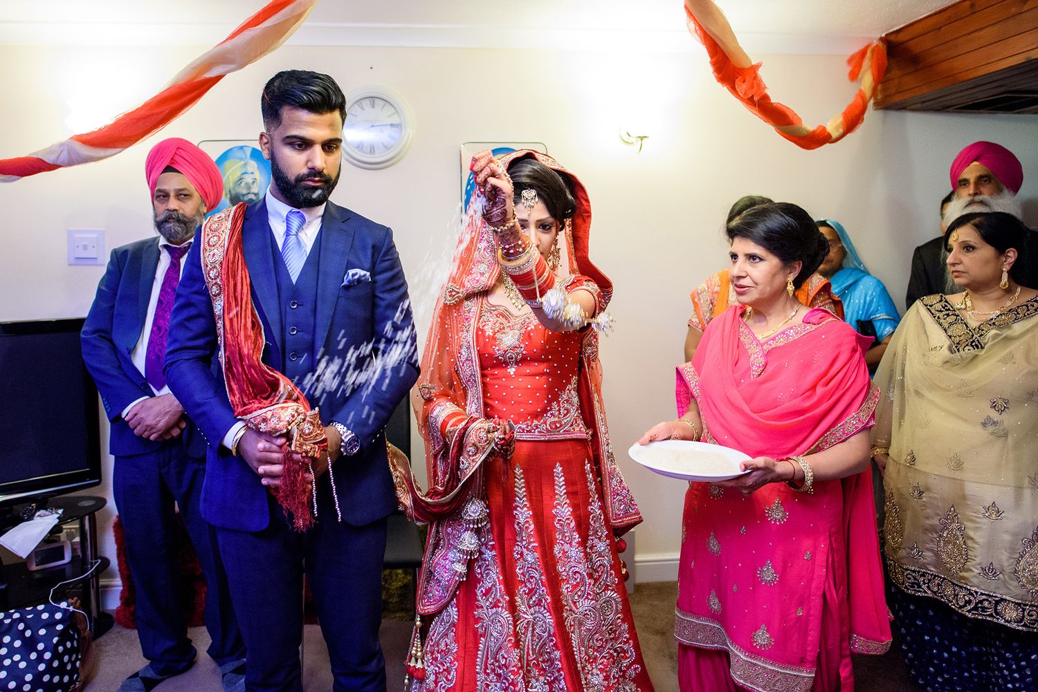 Traditional Indian wedding ceremony participants in colorful attire gathered indoors for religious rituals.