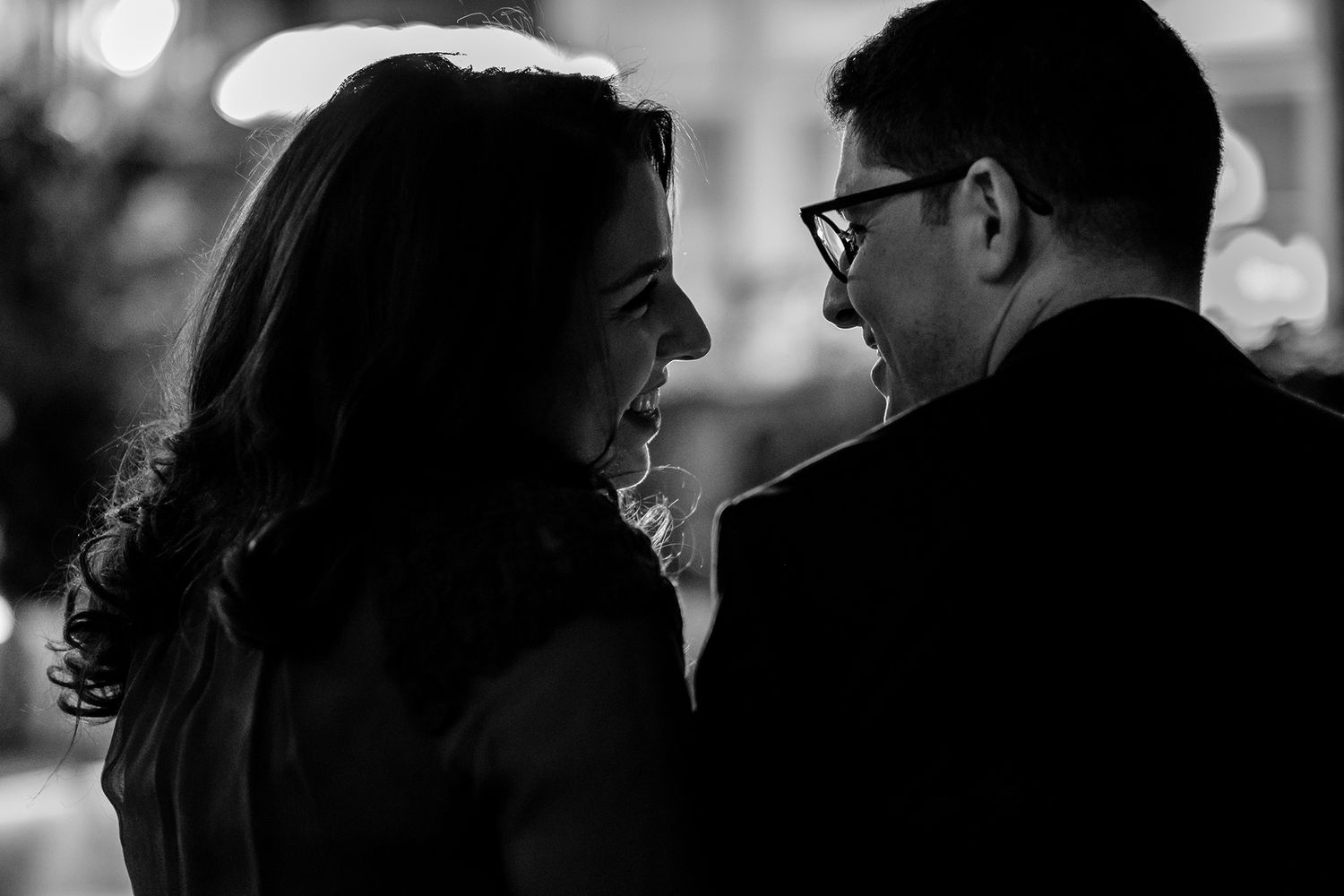 Black and white silhouettes of people embracing at an evening gathering.