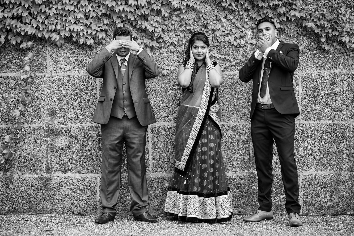 Three people pose playfully against an ivy-covered wall in black and white photography.