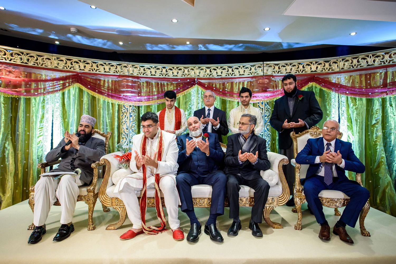 Panoramic view of wedding guests seated along decorated venue with green and red draping.