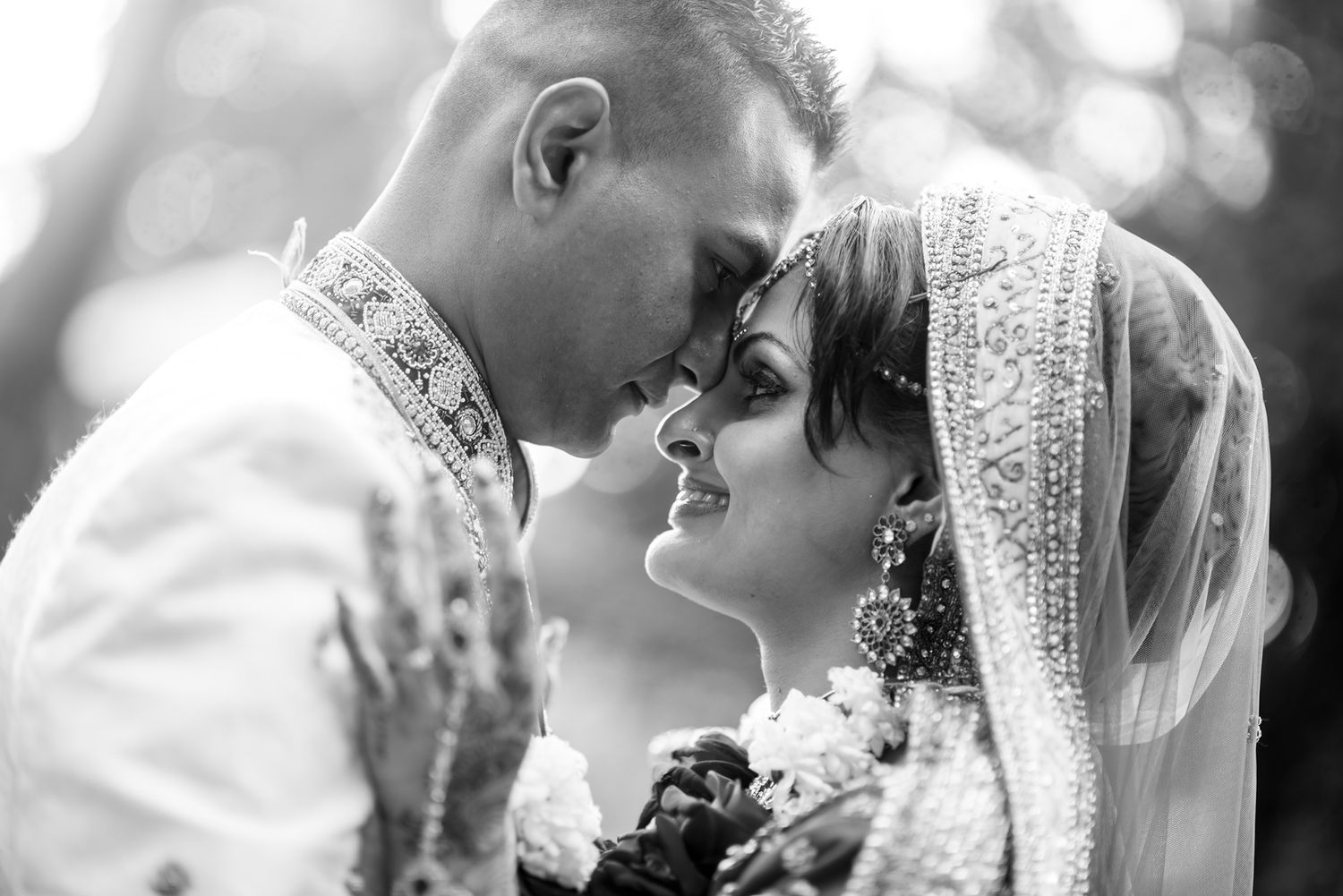An intimate black and white wedding portrait of a couple in traditional South Asian attire sharing a romantic moment.
