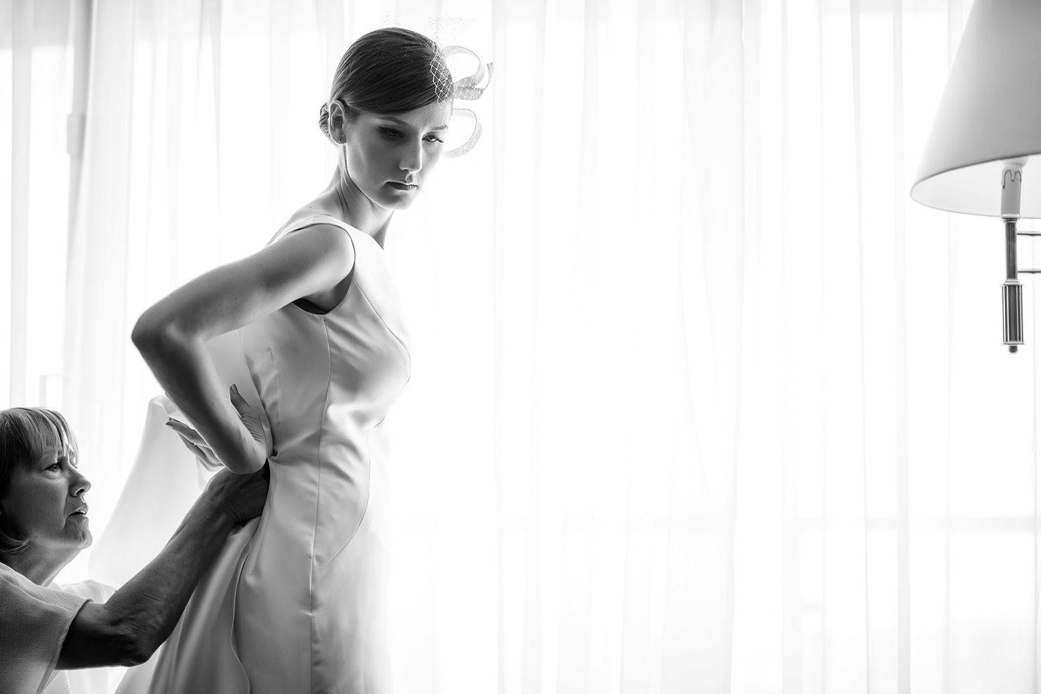 Wedding dress silhouette against bright window light in luxurious hotel room.