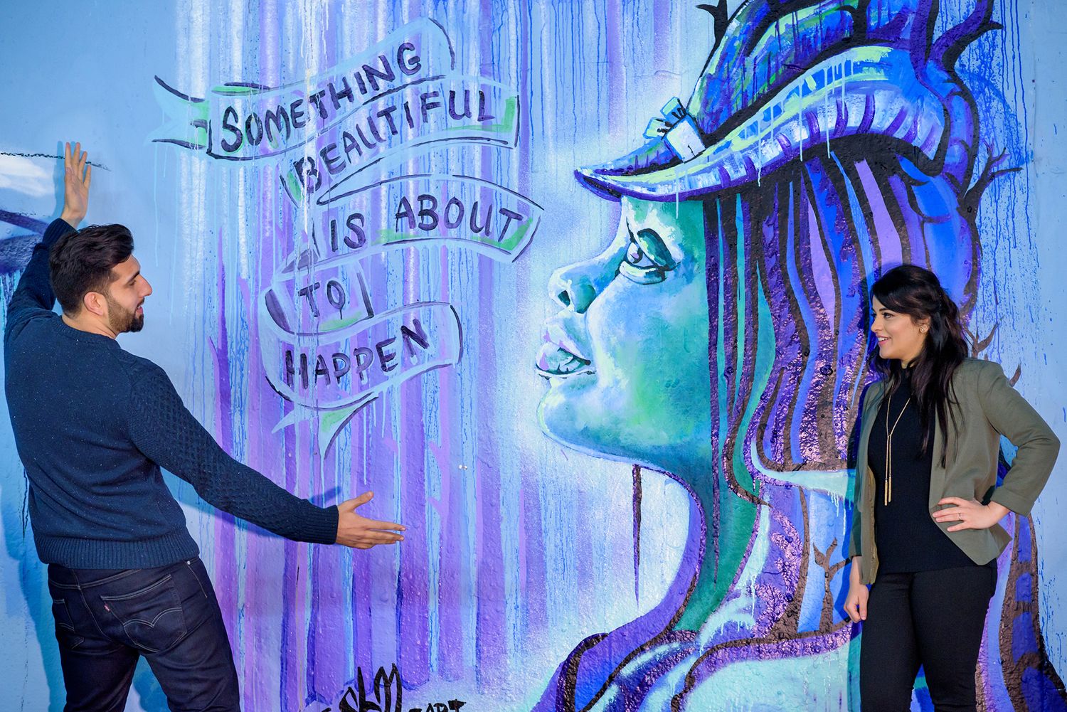 Couple poses near blue-tinted street art with mystical sea creature designs.