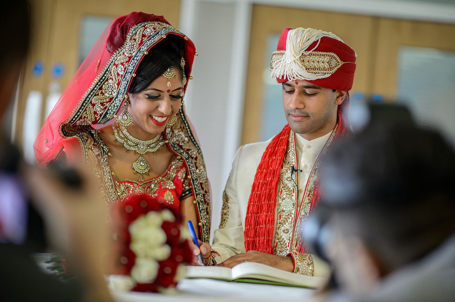 Wedding ceremony participants in traditional red and gold attire signing documents.