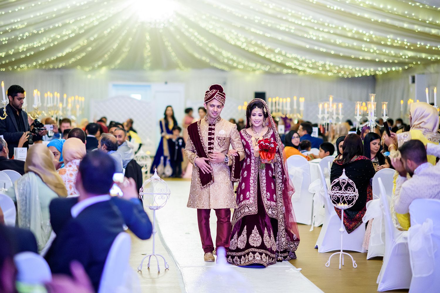 Elegant wedding reception under a tent with sparkling string lights and traditional Indian attire.