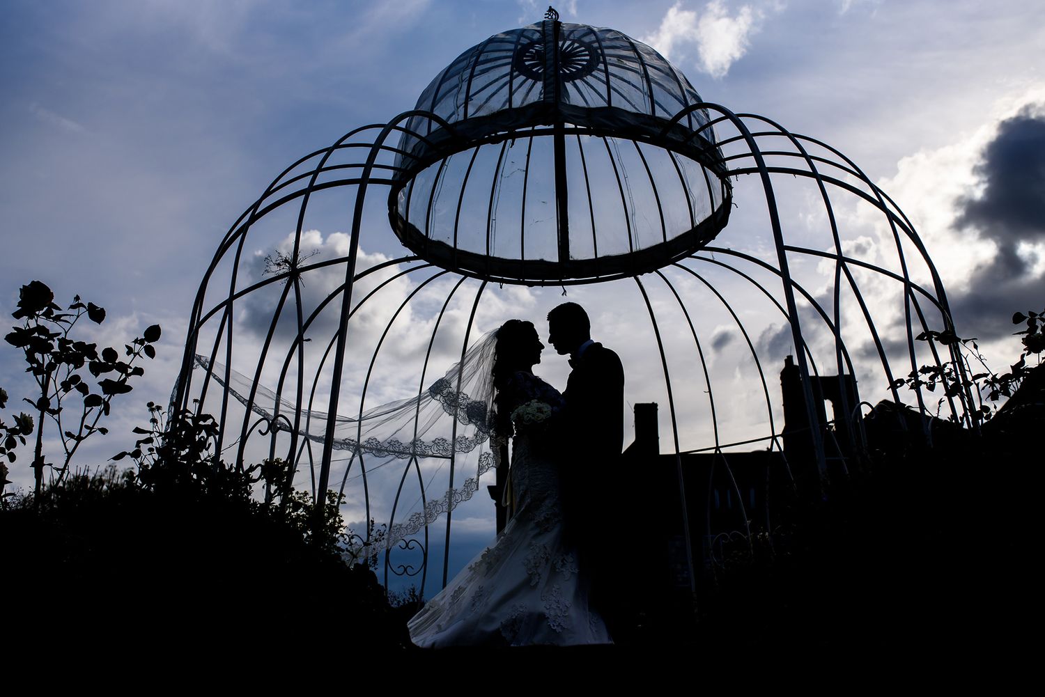 Silhouettes of decorative garden structures against a dramatic cloudy sky at dusk.