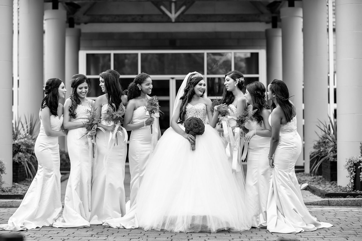 Row of white wedding dresses lined up in classical columned venue.