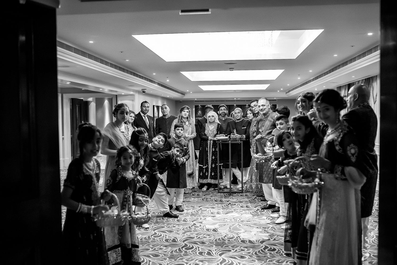 Monochrome wide view of guests gathered for a wedding reception with skylight ceiling.