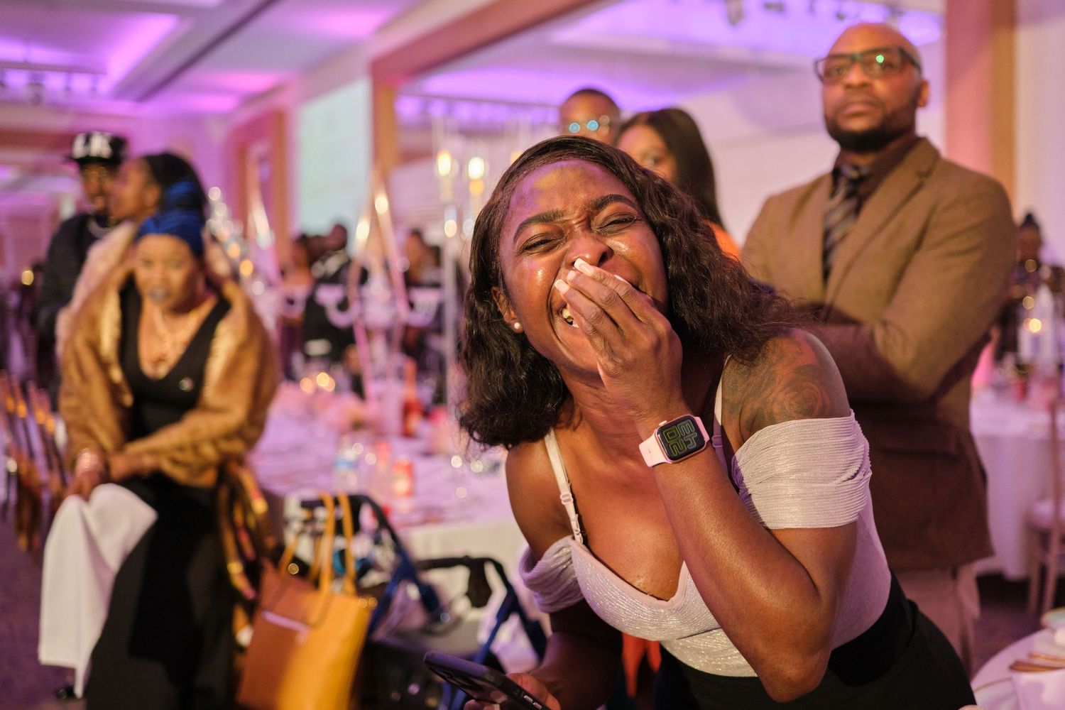 People dancing and celebrating at a wedding reception with pink and purple lighting in an elegant ballroom setting.