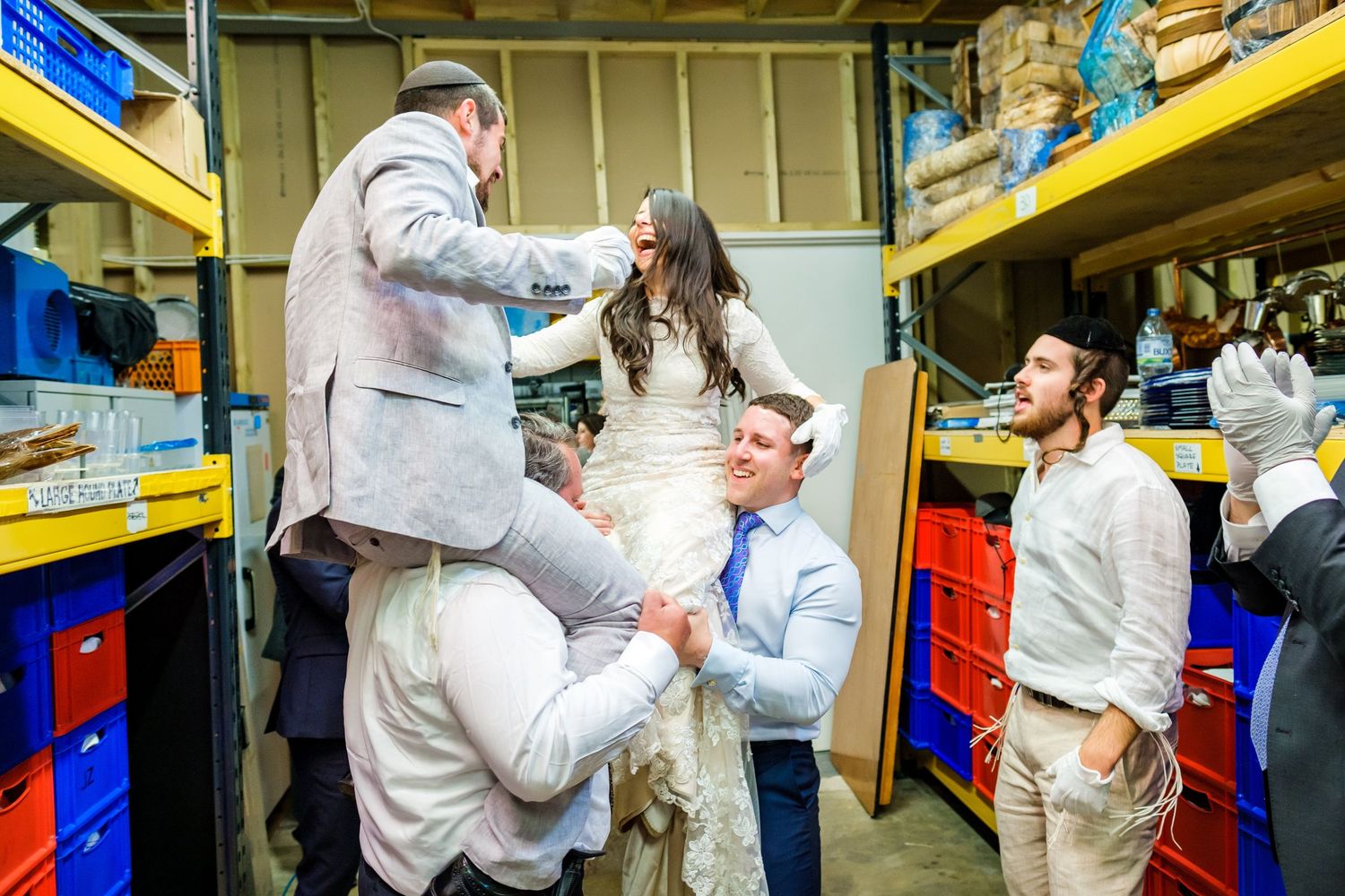 Group dancing and celebrating in a storage room with yellow shelving units.