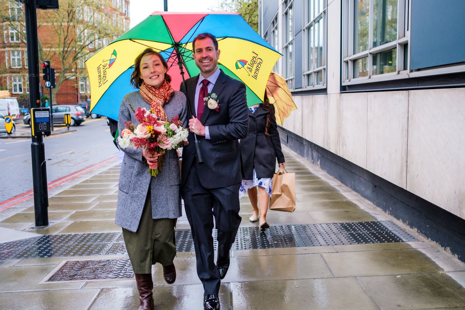 Couple walking together under bright umbrellas along a wet city sidewalk with flowers.
