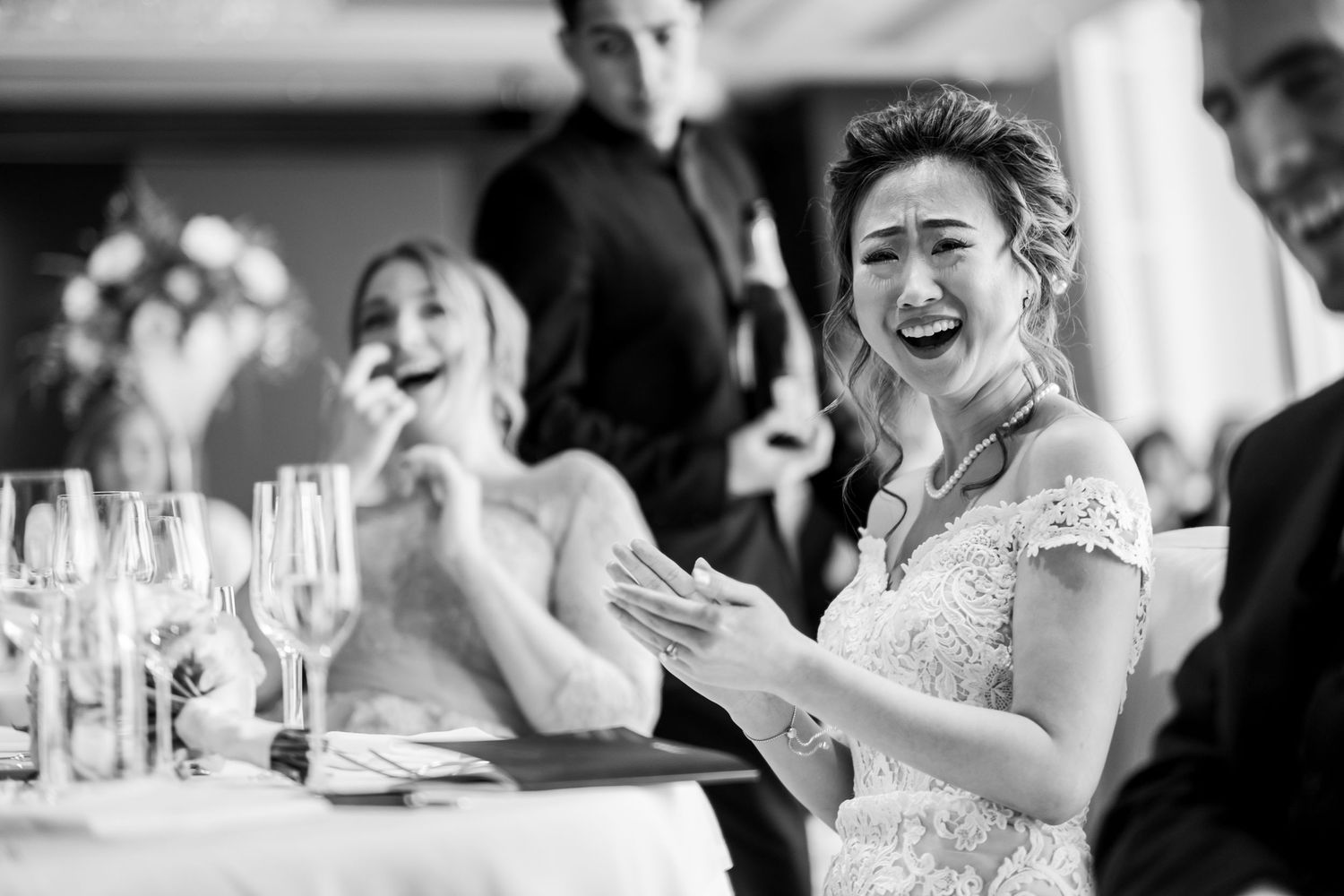 Black and white candid wedding reception photos showing guests laughing and celebrating at tables.