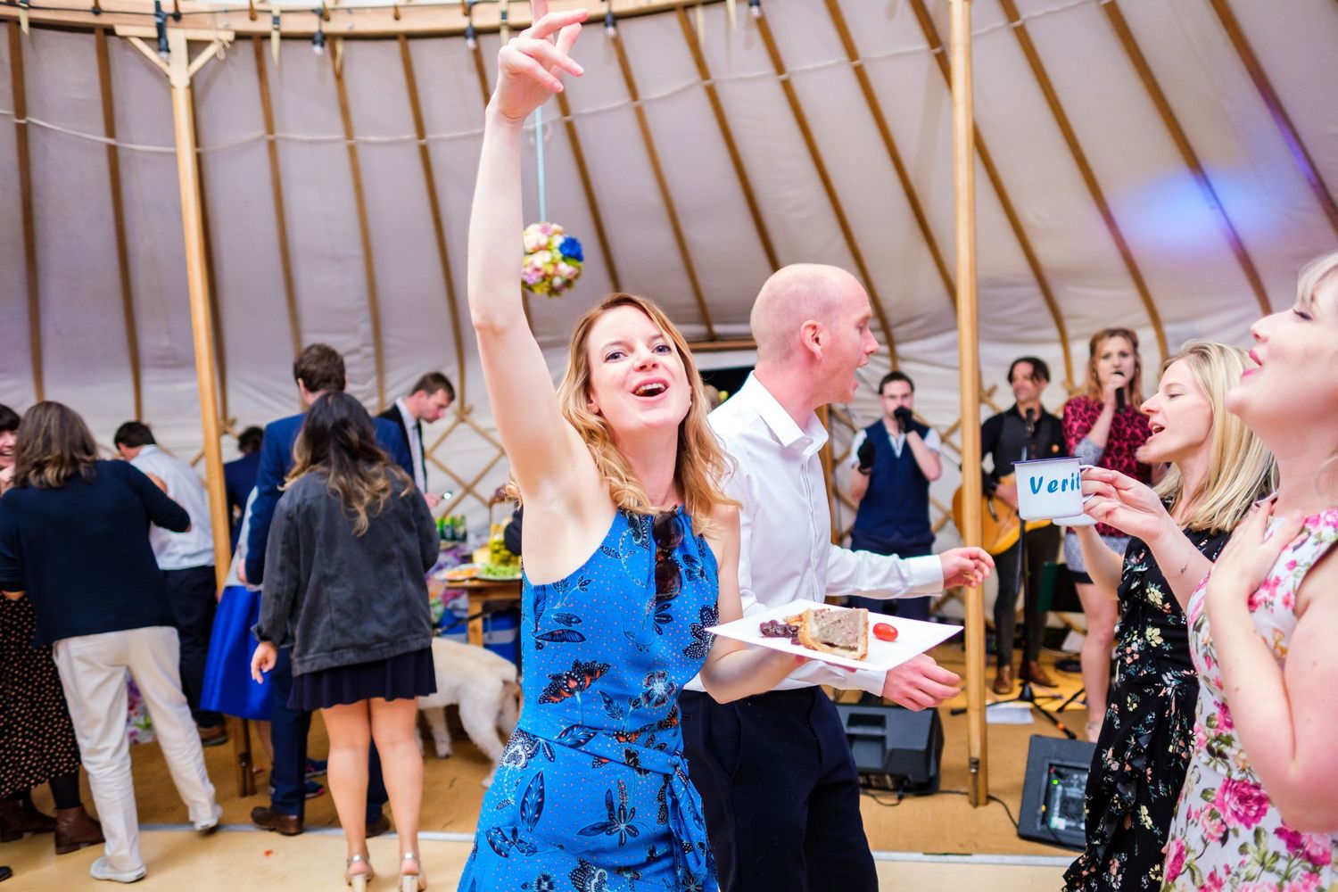 Wedding guests dance and celebrate inside a rustic yurt venue during a lively reception.