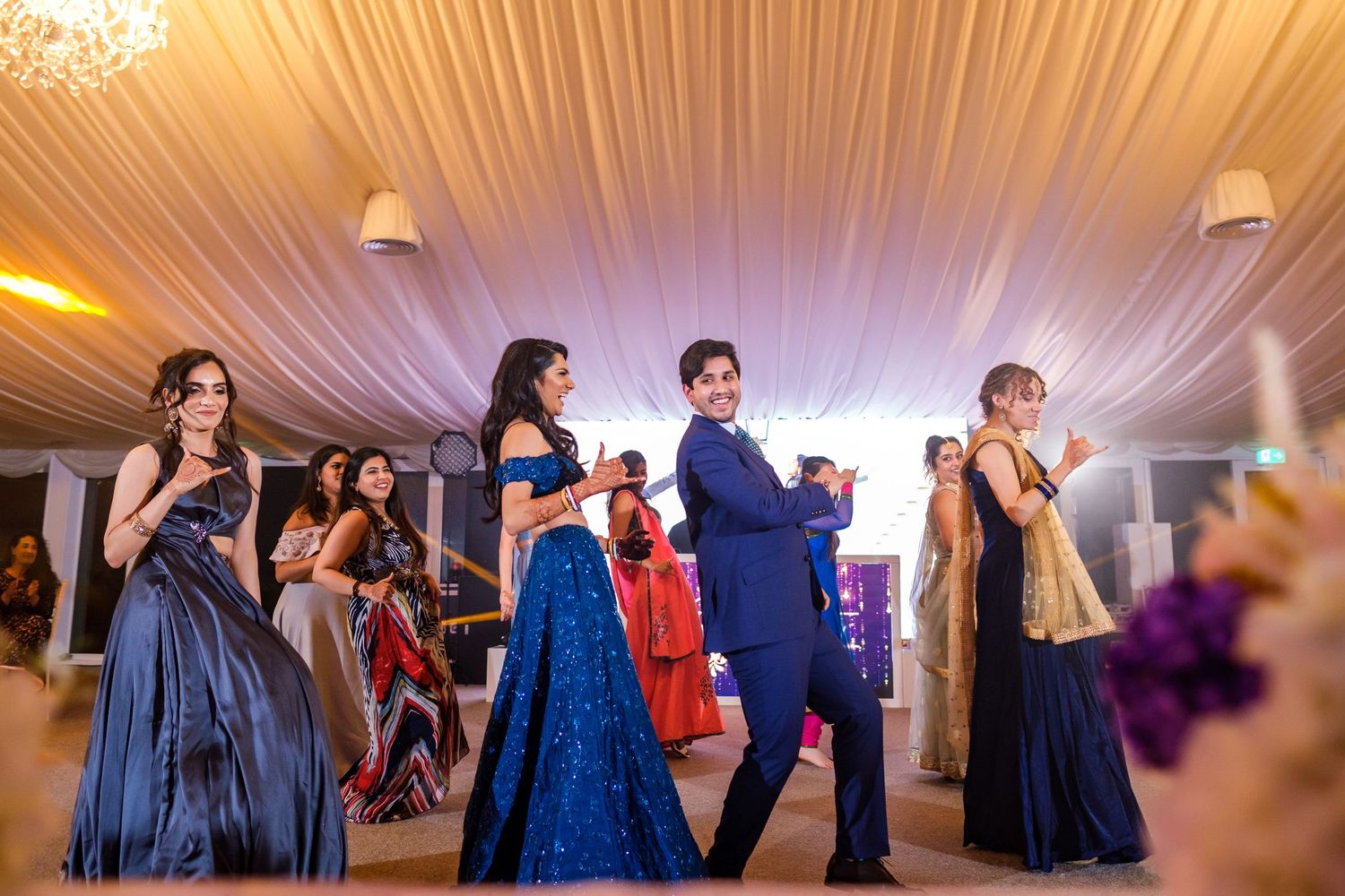 Wedding guests dancing and celebrating in a beautifully lit white tent reception space.