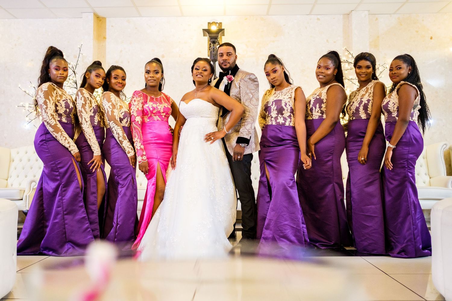 Large bridal party lined up in purple dresses for formal wedding photo.