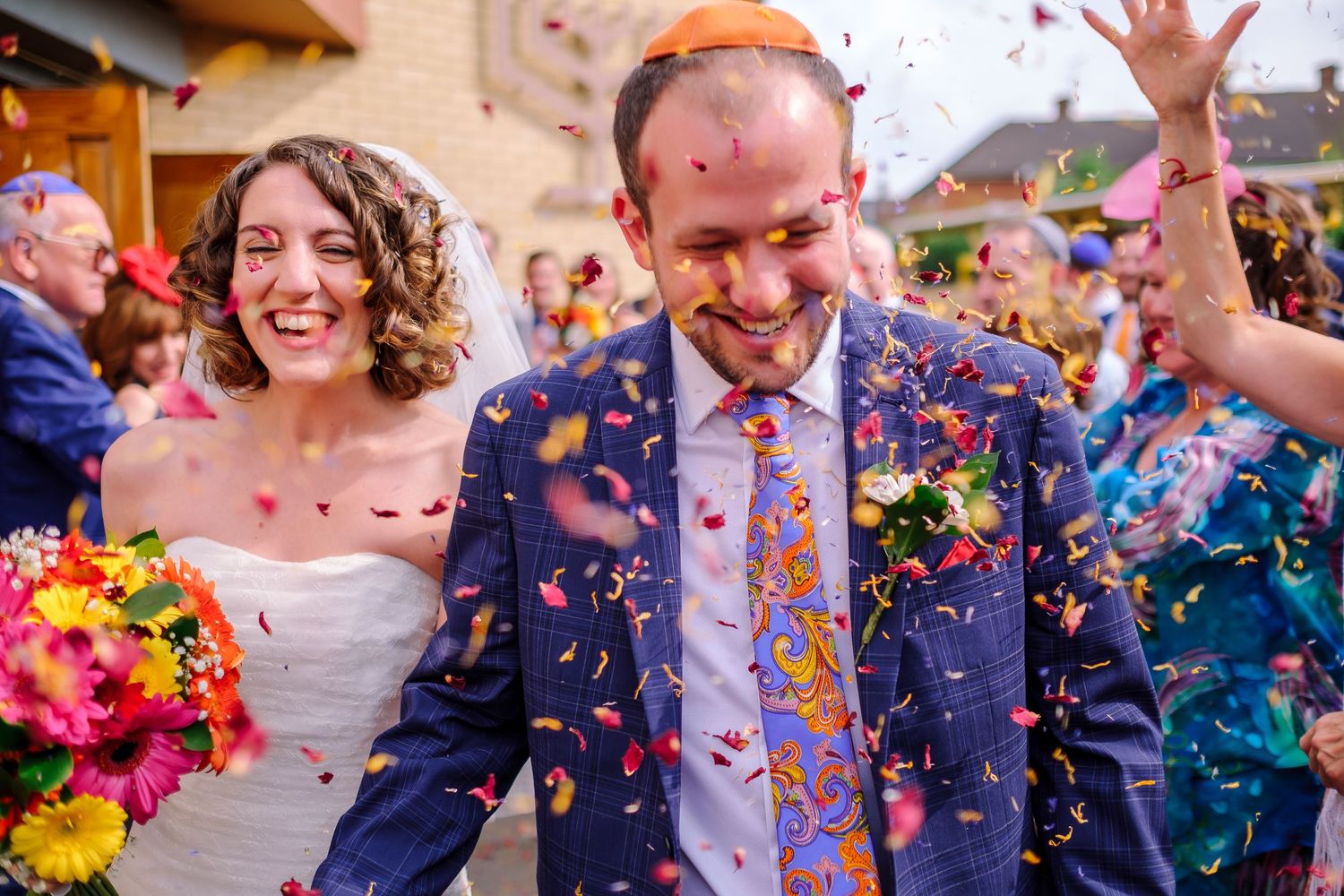 Joyful wedding celebration with colorful confetti being thrown in outdoor setting.