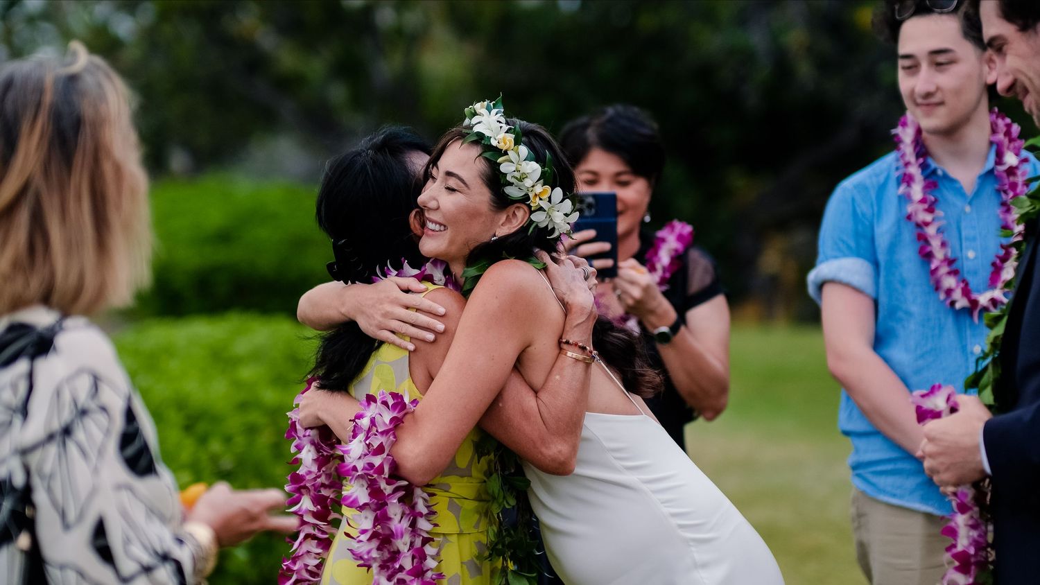 Emotional embrace during a Hawaiian wedding celebration with guests wearing traditional leis.