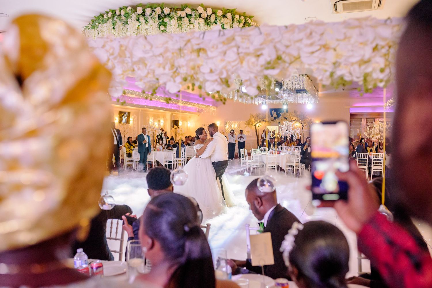 Wedding guests capture a couple's first dance under crystal chandeliers at an elegant reception.