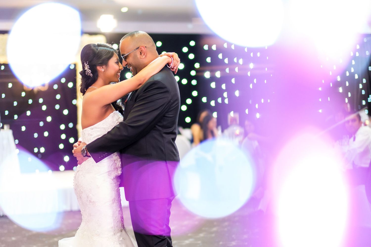 Romantic first dance at wedding reception with purple and blue lighting effects.
