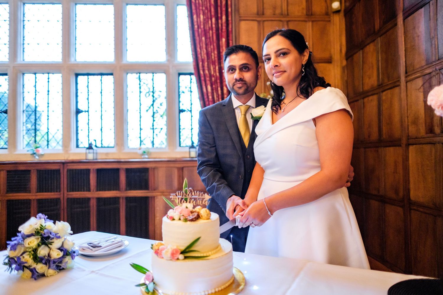 Wedding reception venue interior with elegant red curtains and wooden paneled walls during cake cutting ceremony.