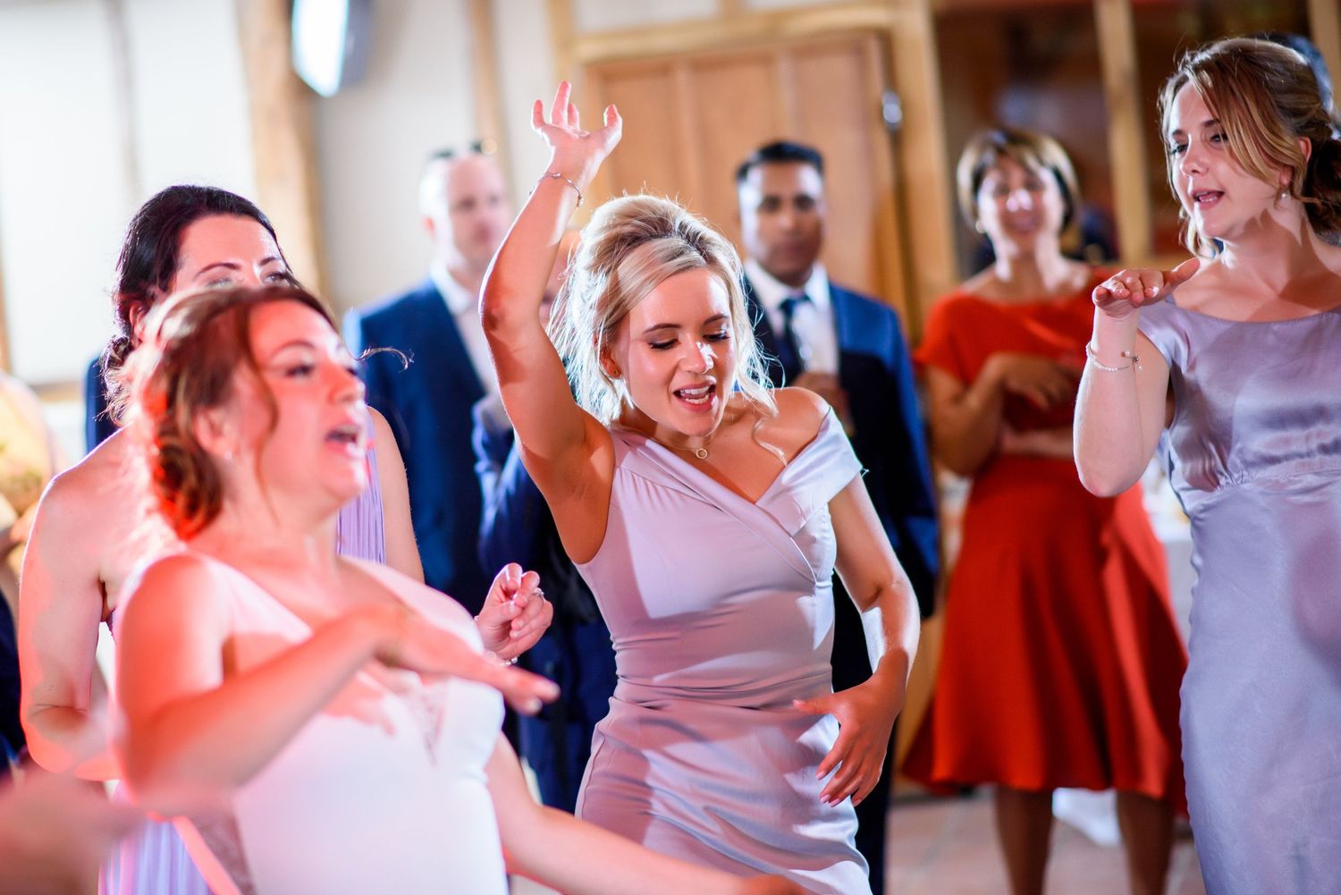 Wedding guests dance and celebrate joyfully on a lively dance floor illuminated with colorful lighting.