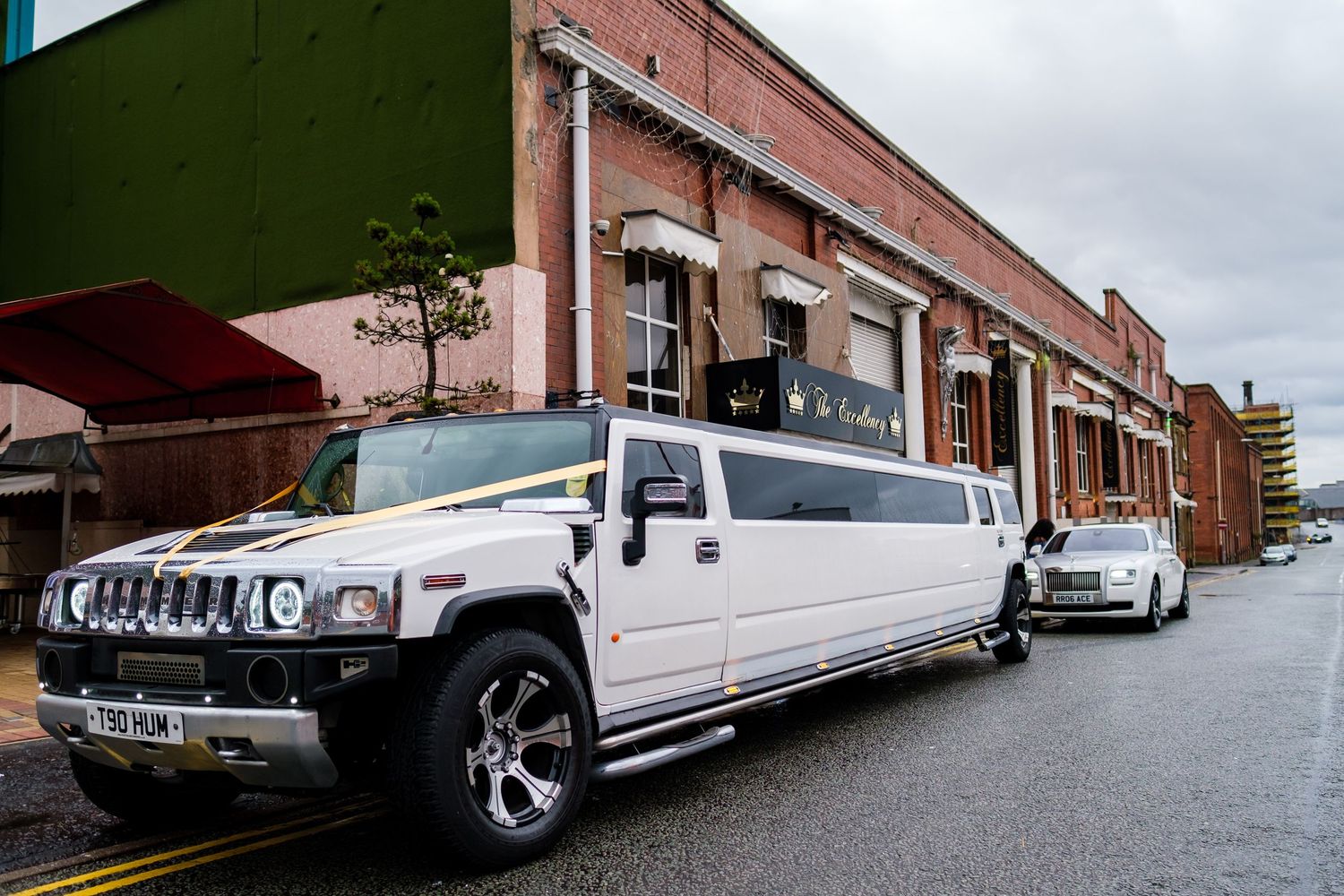 Row of white stretch limousines parked outside a brick building.