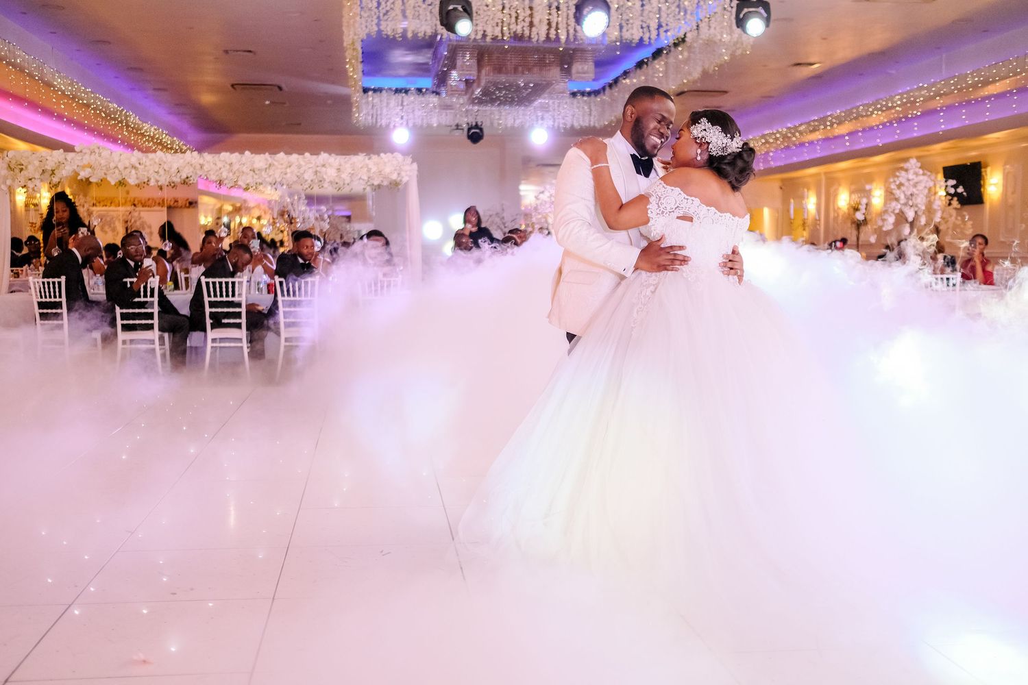 Elegant ballroom wedding reception with purple lighting and white decor.