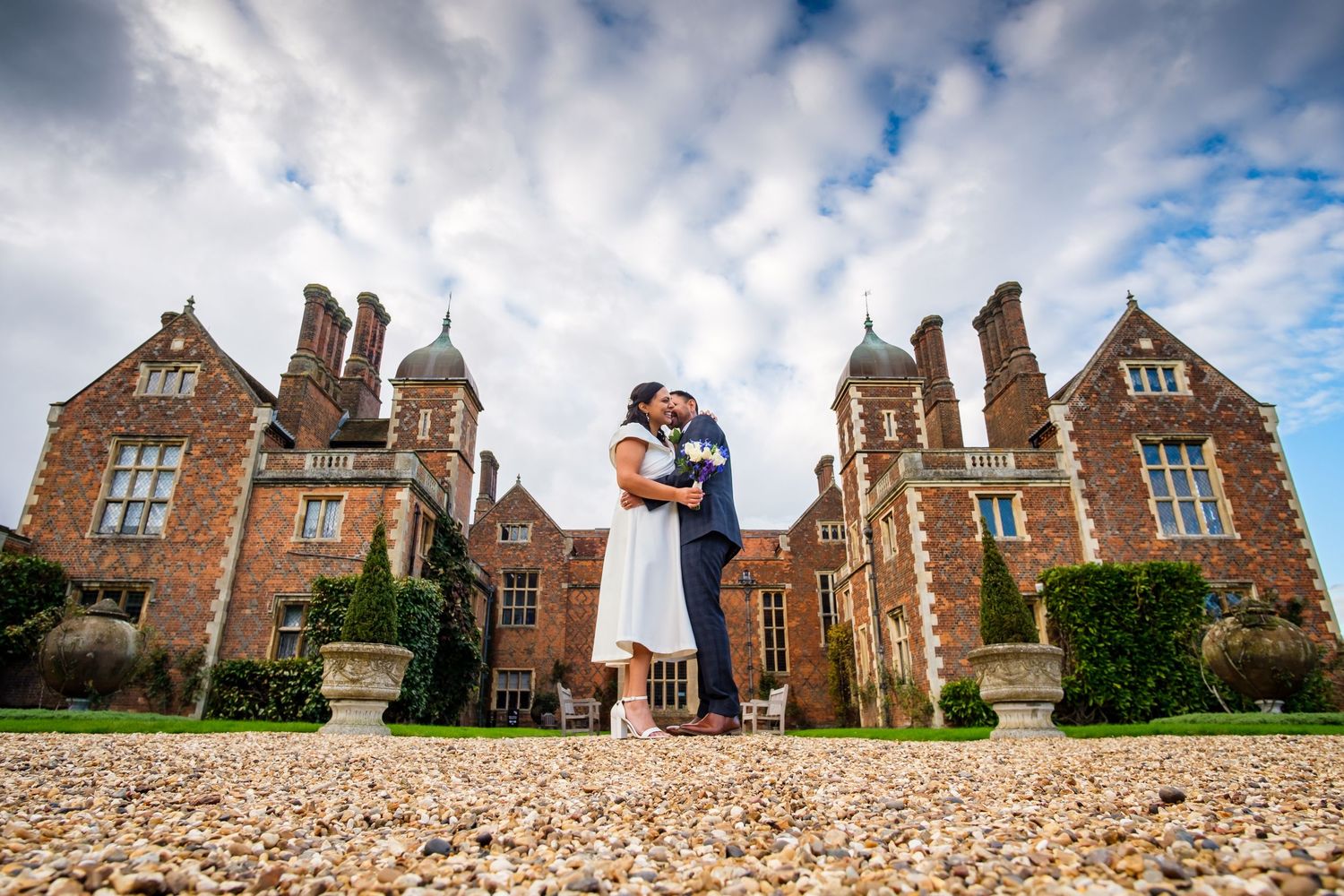 Panoramic view of a grand historic brick mansion with dramatic cloudy sky backdrop.