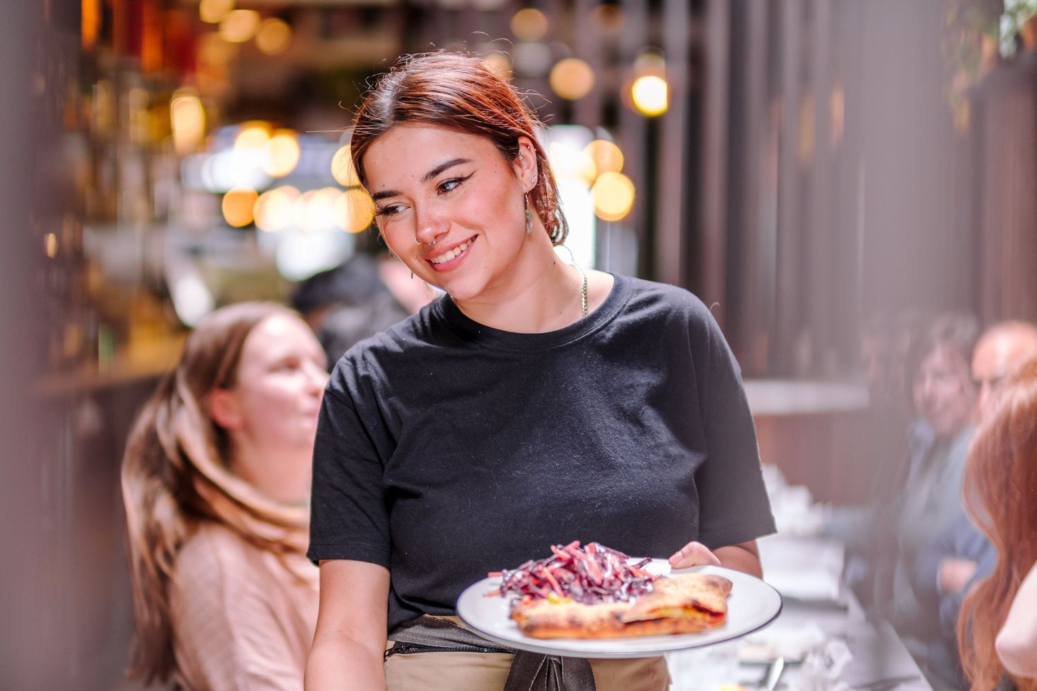 Restaurant staff serving fresh pizzas to customers in a warmly lit dining room.