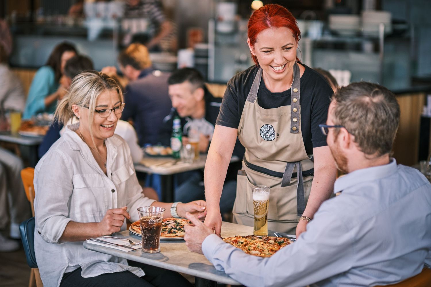 Customers enjoying food and conversation at restaurant tables with warm lighting.