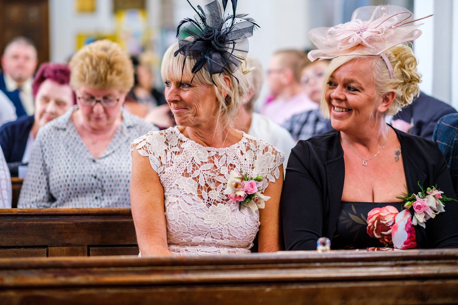 Wedding guests seated in church pews smile and laugh during ceremony.