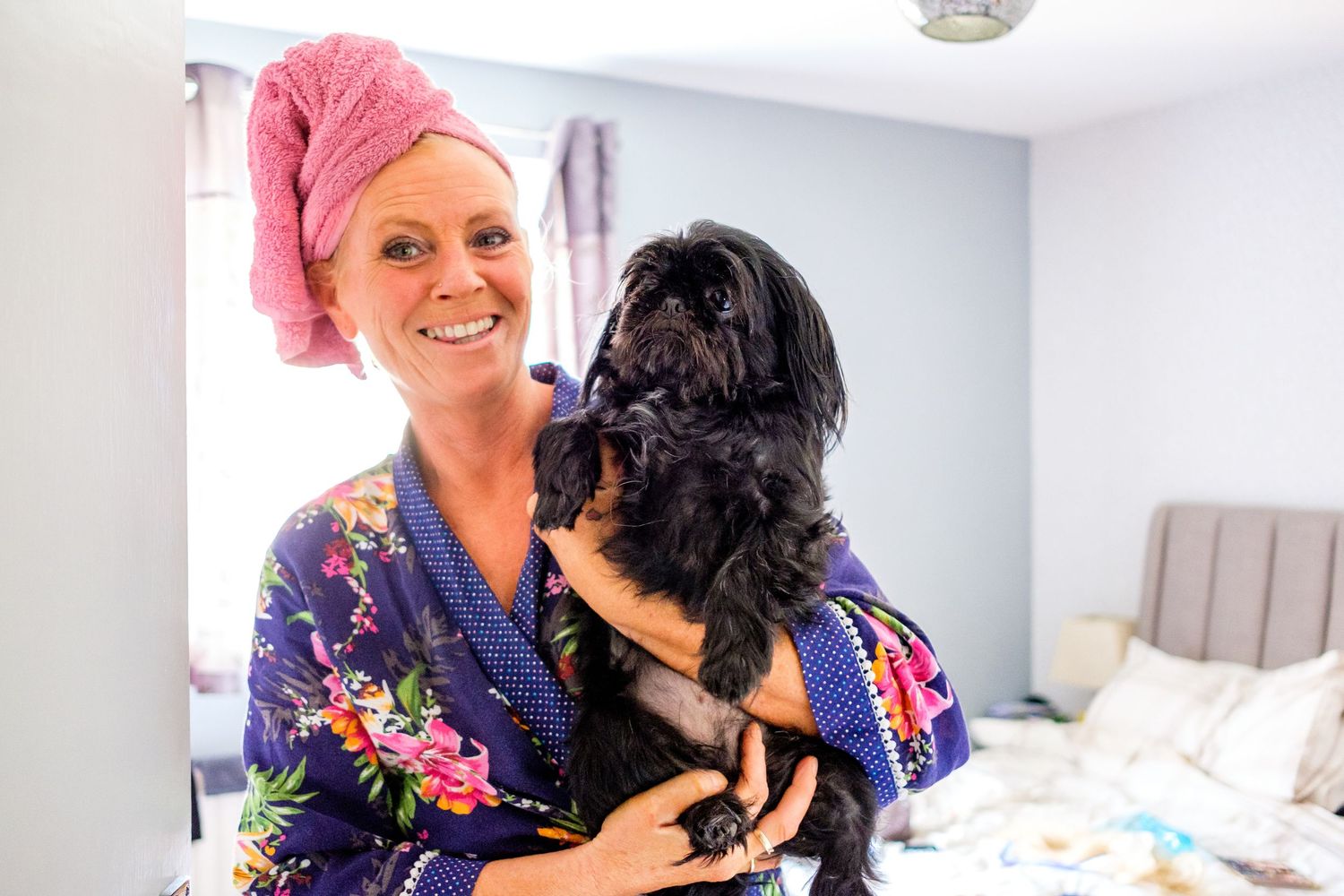 A black dog gives loving kisses while being held in someone's arms wearing a colorful top.