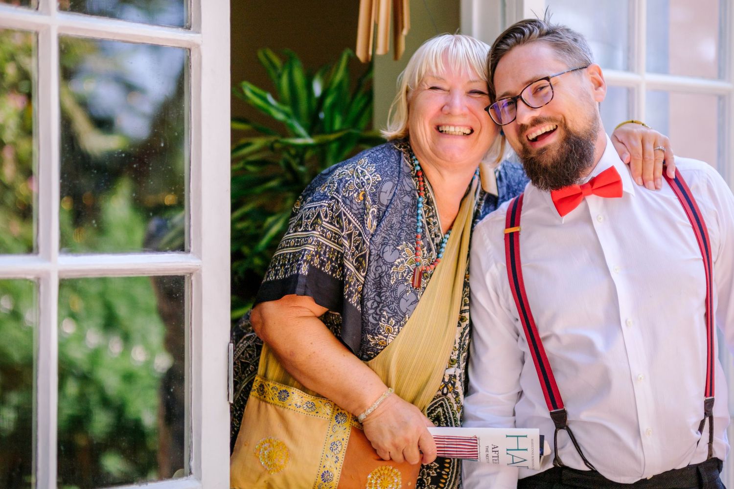 A couple shares a joyful moment together wearing coordinated formal attire with red accents and suspenders.