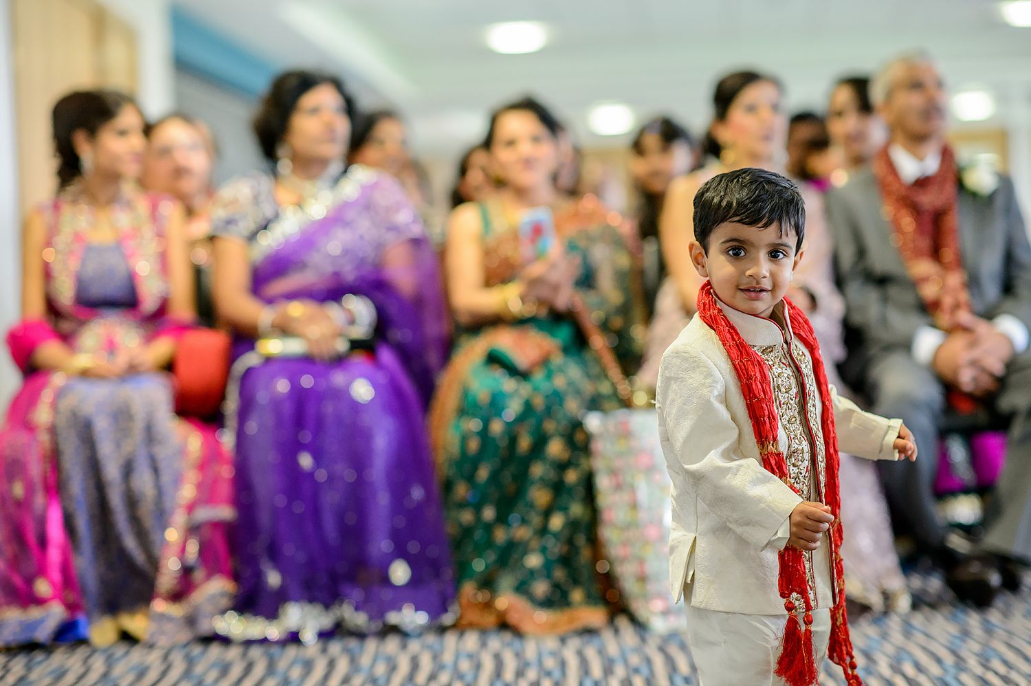 Wedding guests in vibrant traditional Indian attire gathering at indoor celebration venue.