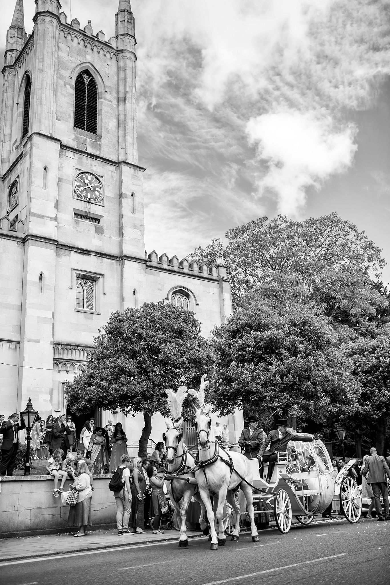 Wedding party and horse drawn carriages outside gothic church on cloudy day.