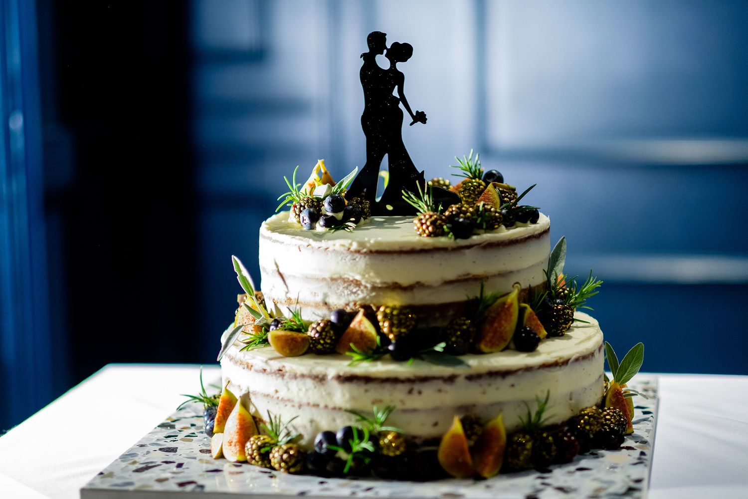 Wedding cake displayed on white tablecloth with decorative greenery and silhouette cake topper.
