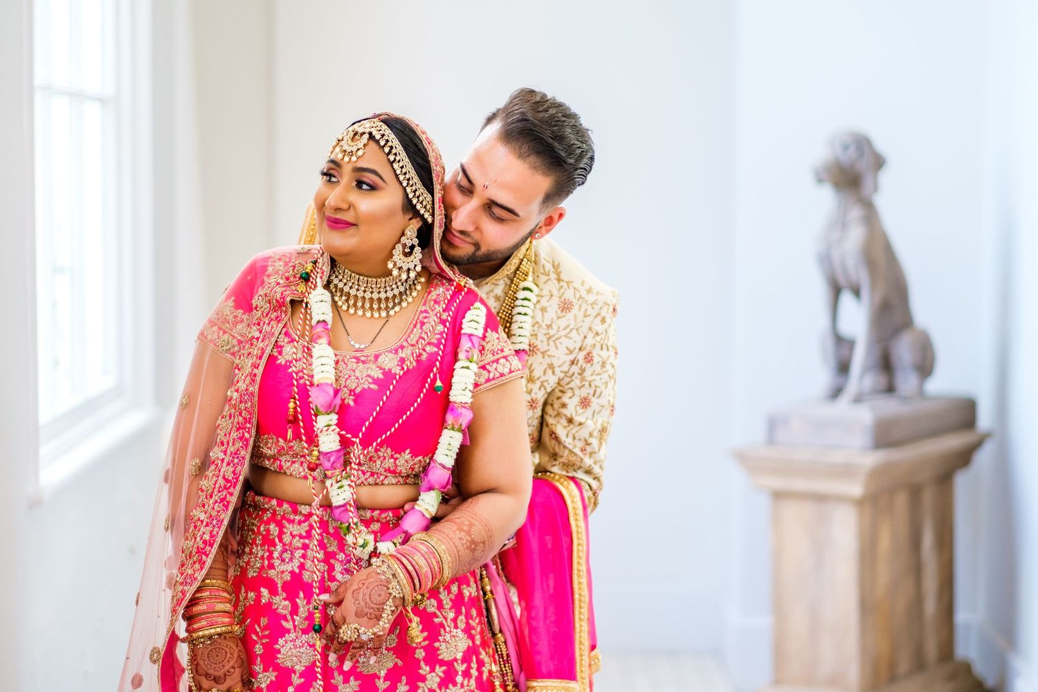 Couple in traditional Indian wedding attire share intimate moments in an elegant indoor setting.