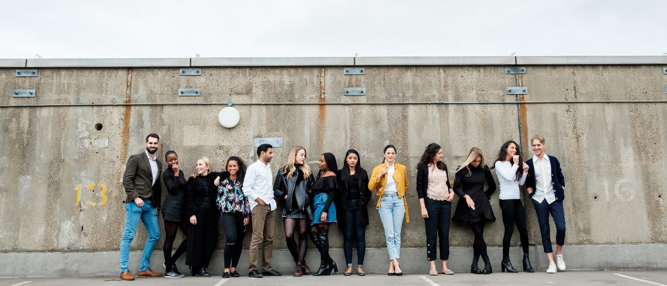 Long line of people standing against a concrete wall outdoors.