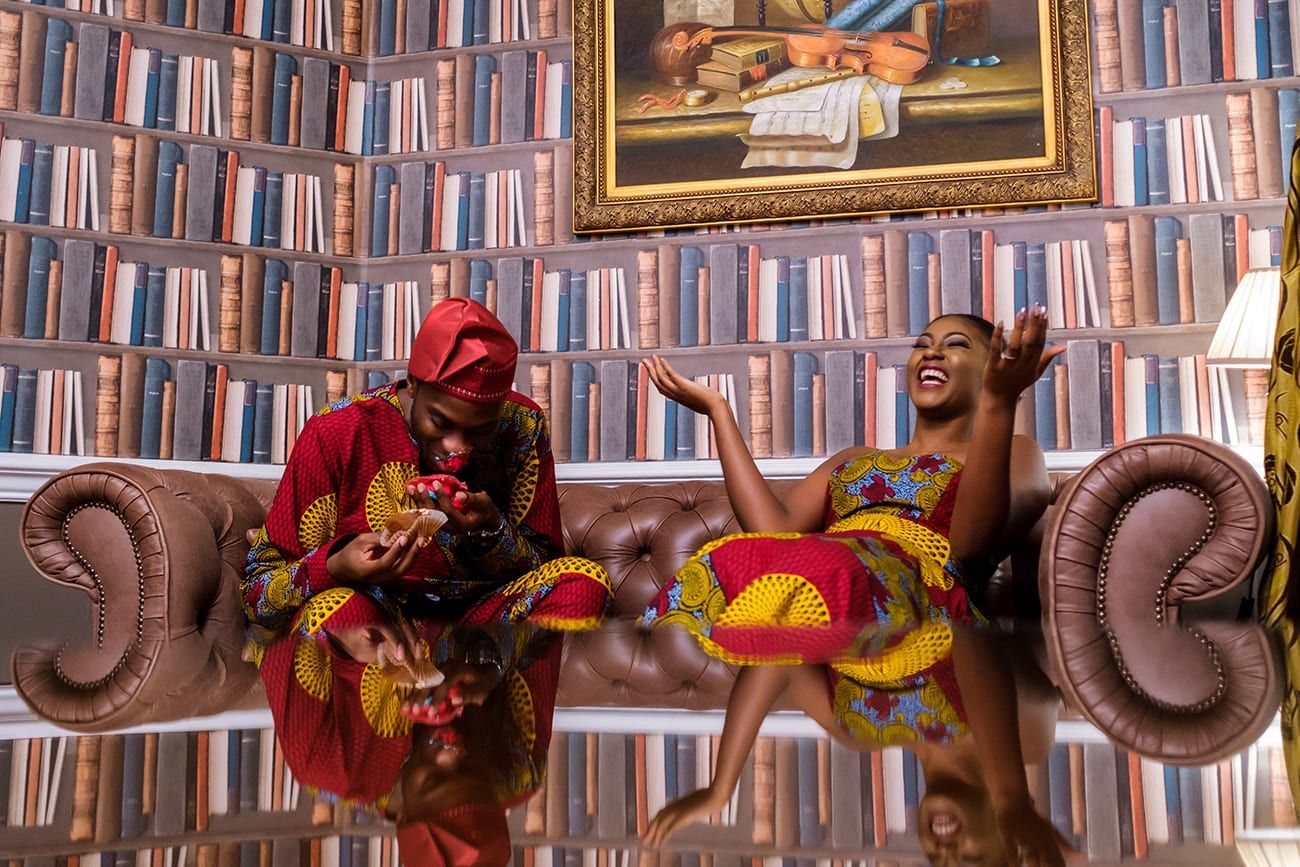 Women in vibrant African print dresses pose together on brown leather couch.