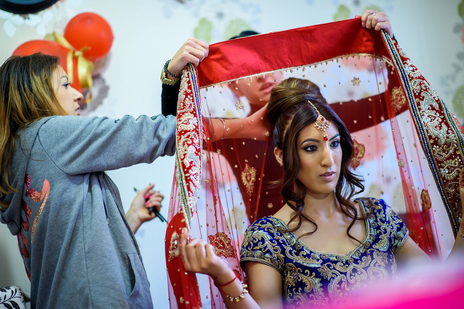 A person in a grey shirt adjusts a red bridal veil during wedding preparations.