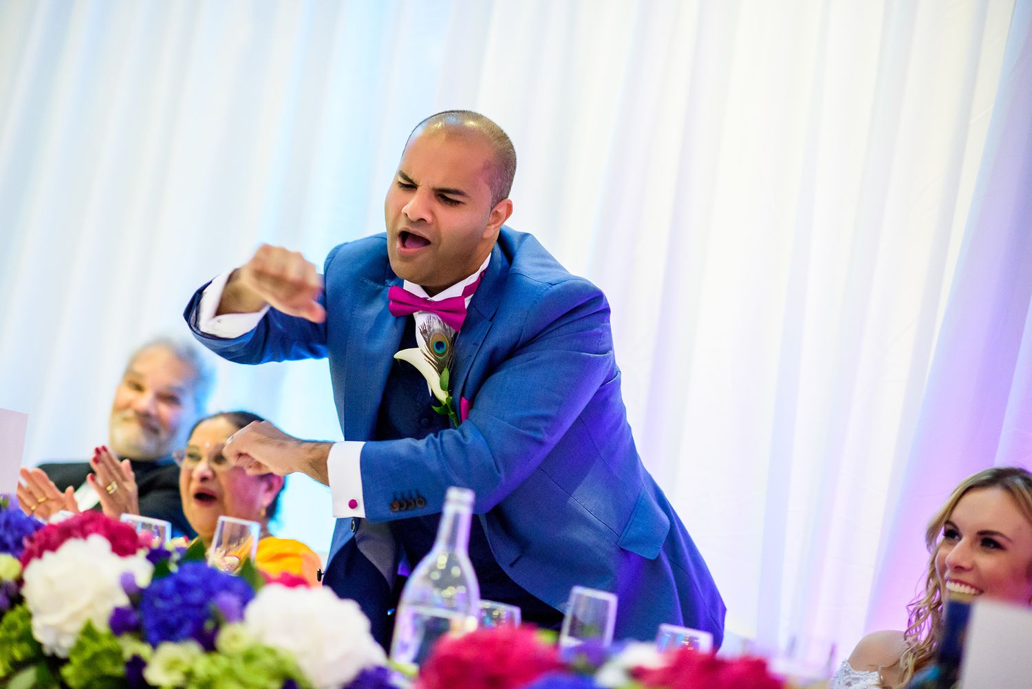Wedding reception guests enjoying drinks and celebrating at an elegant venue with chandelier lighting.