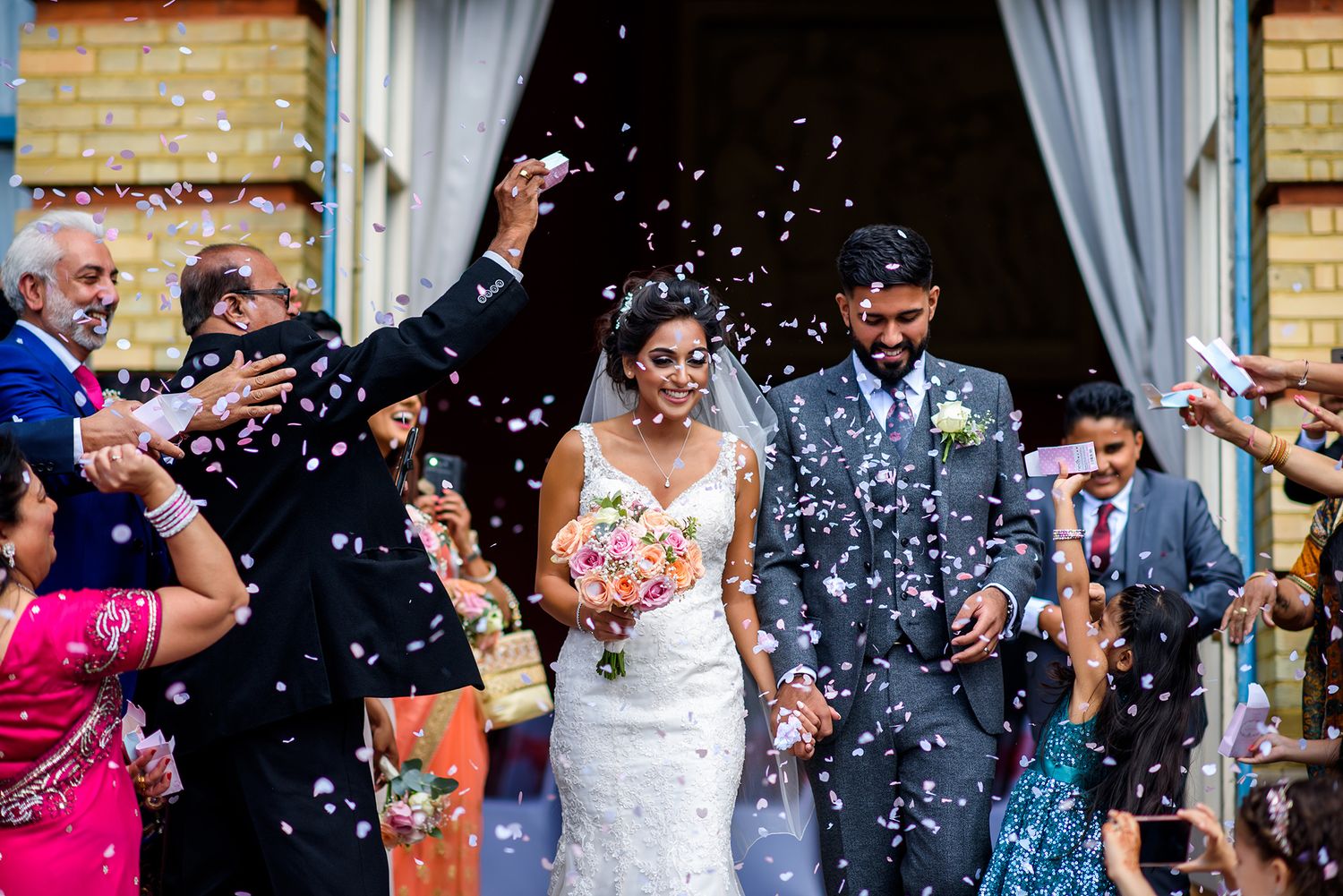 Wedding guests throw white confetti at the newlyweds during outdoor celebration.