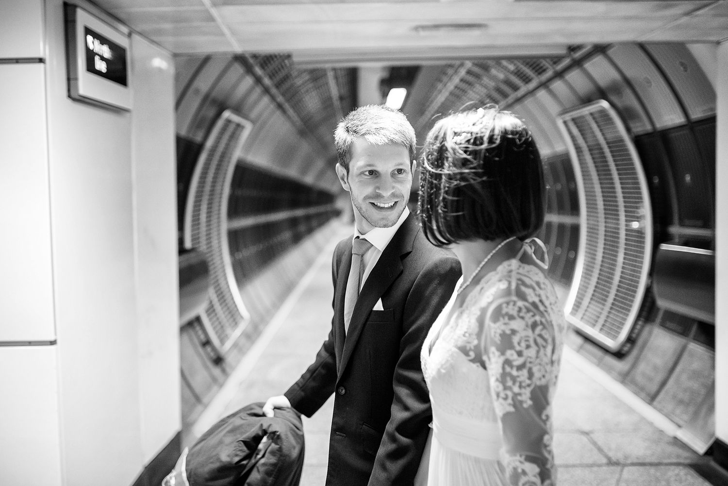 Black and white photo of couple walking through a modern tunnel with geometric lighting.