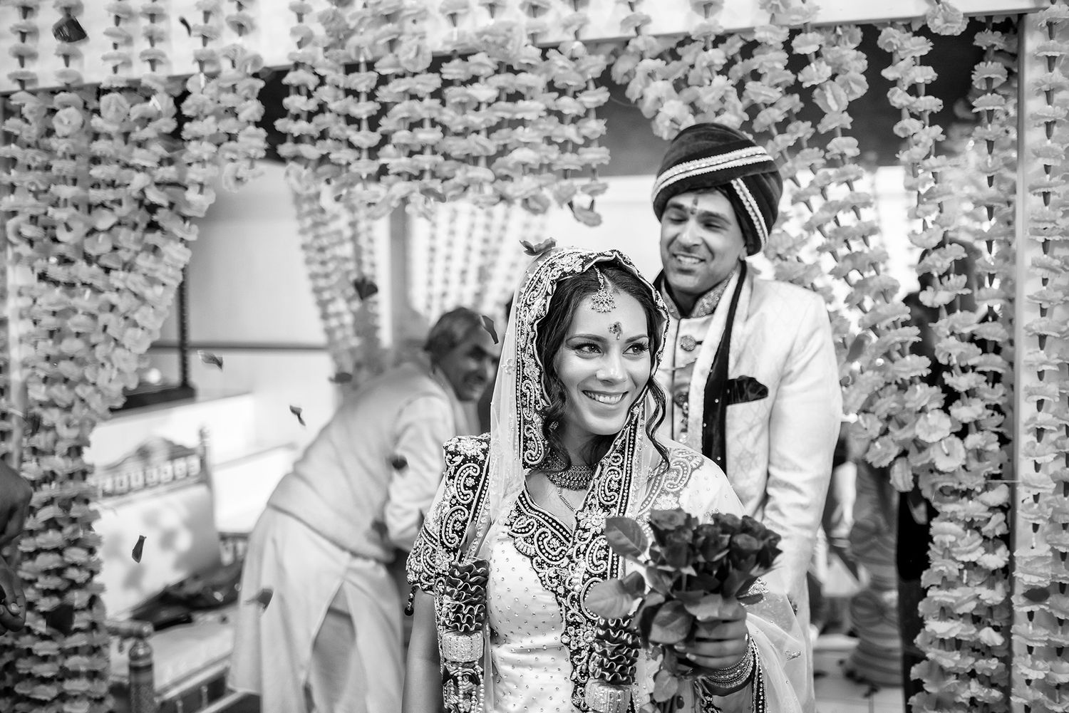 Black and white photo of traditional Indian wedding ceremony with hanging floral decorations.