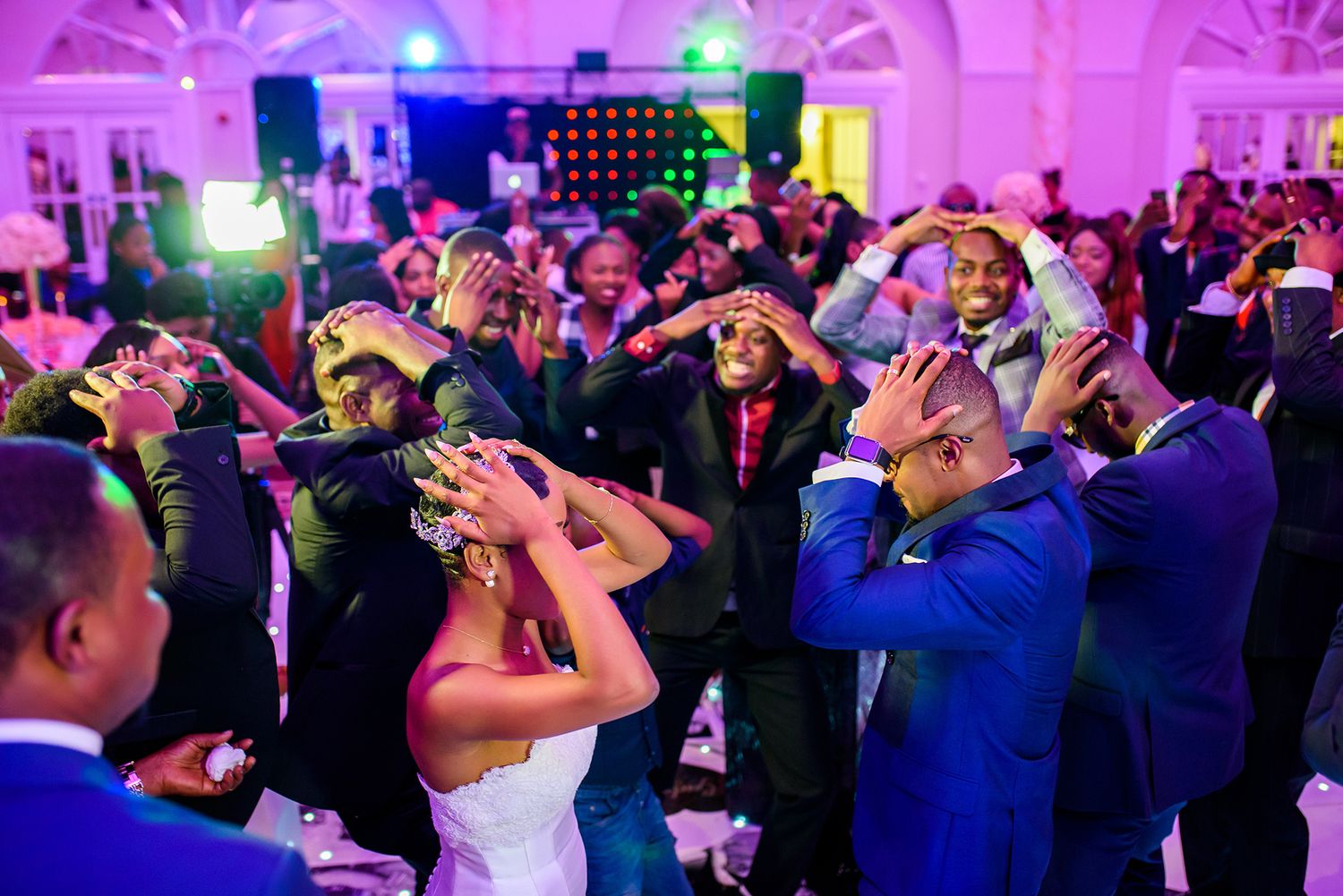 Lively wedding reception dance floor filled with guests under vibrant purple lighting.
