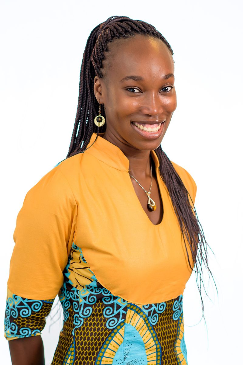 Woman in bright yellow and patterned African print dress poses confidently against white background.