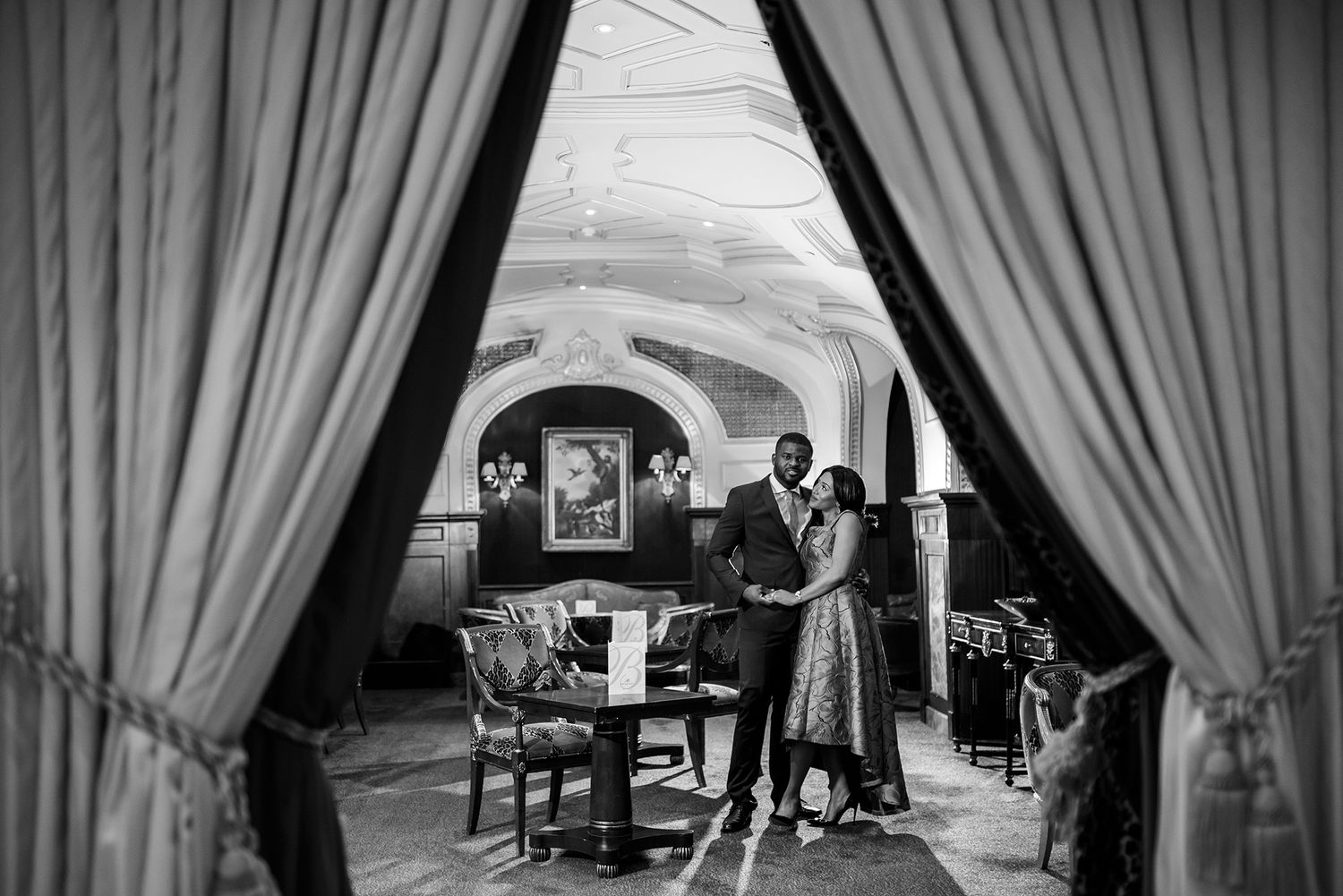 Black and white photo of formal event space with dramatic curtains.