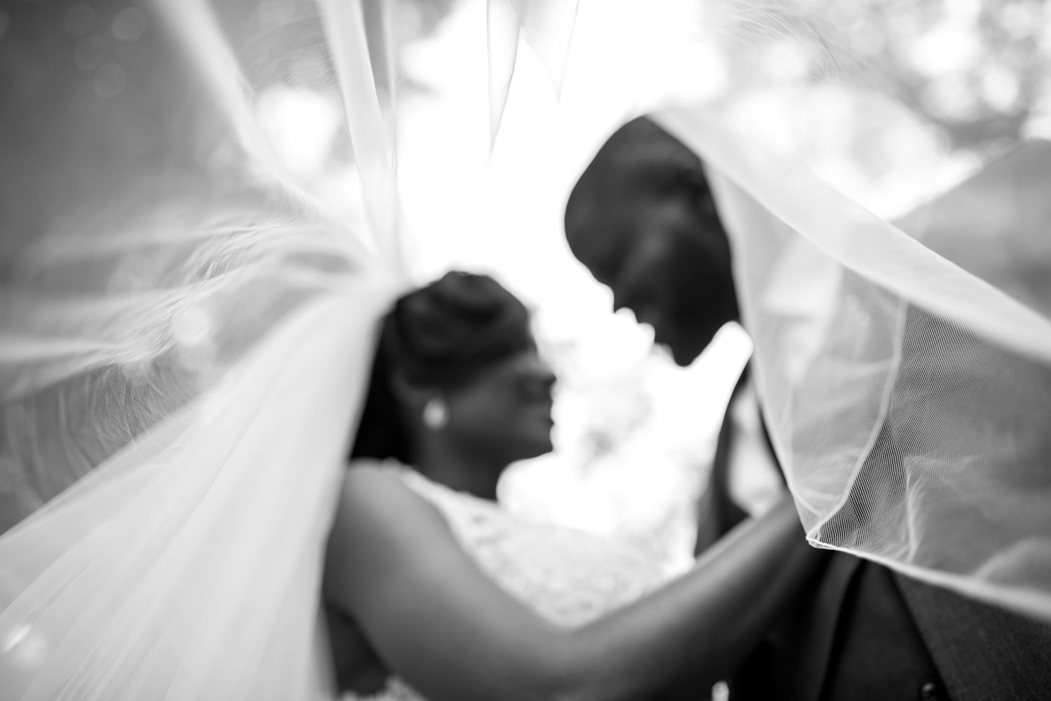 Artistic black and white portraits of a couple under a flowing wedding veil.