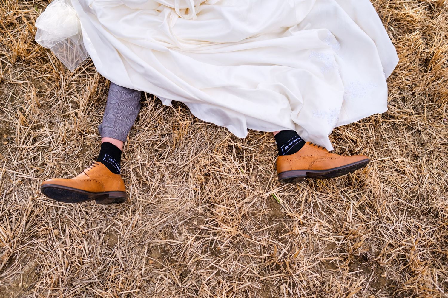 Detail shot of wedding dress train and formal shoes on dried grass.